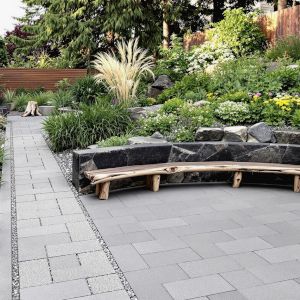 A long garden, paved with grey stone slab, landscaped with large basalt boulders, and planted with a variety of plants including clumping grasses, and echinacea