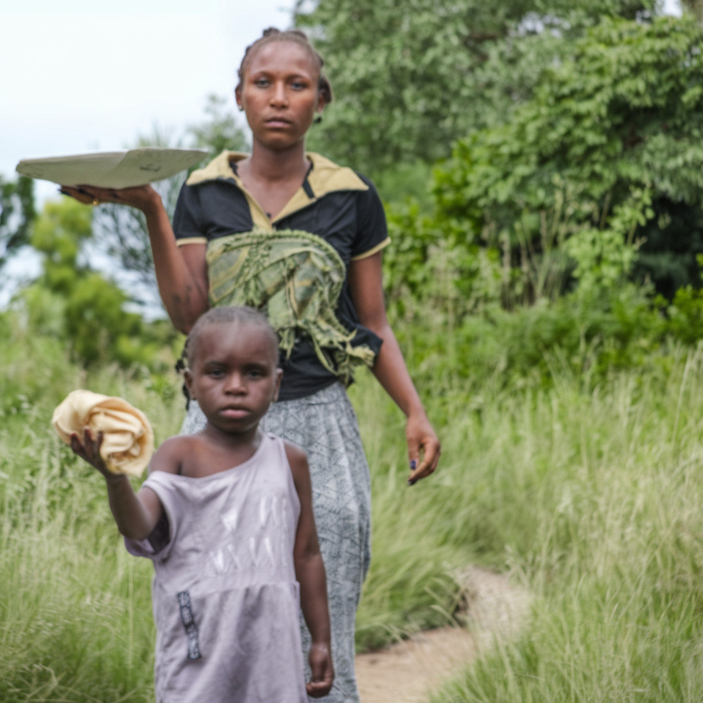 A woman and child walking through lush grass, carrying food.